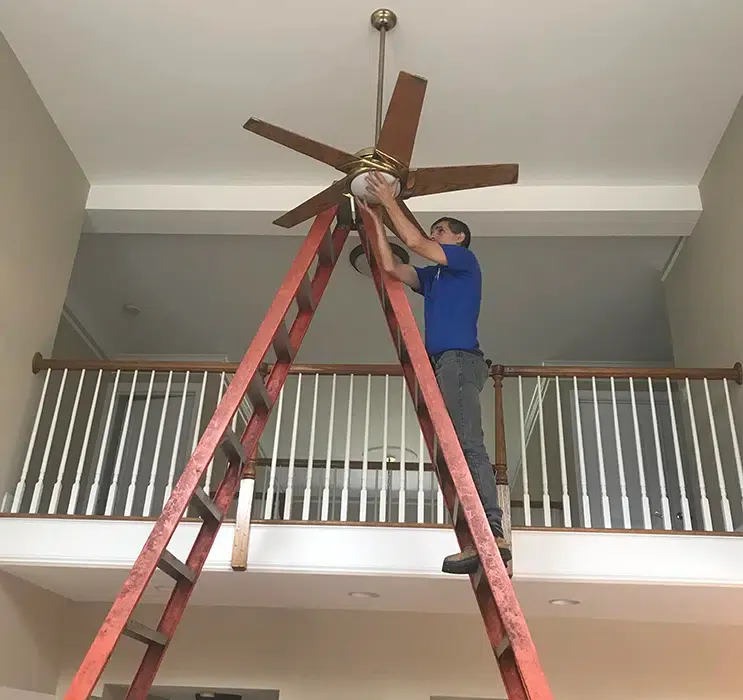 Castle Electric technician installing ceiling fan in Newton MA home from tall A-frame ladder