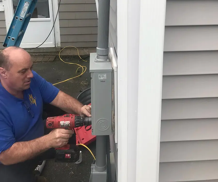 Licensed electrician installing outdoor meter enclosure on Norwood MA home with power drill