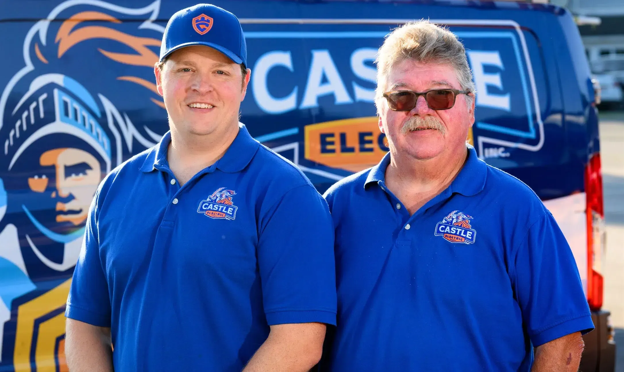 Two Castle Electric owners in branded uniforms standing in front of a company service van.