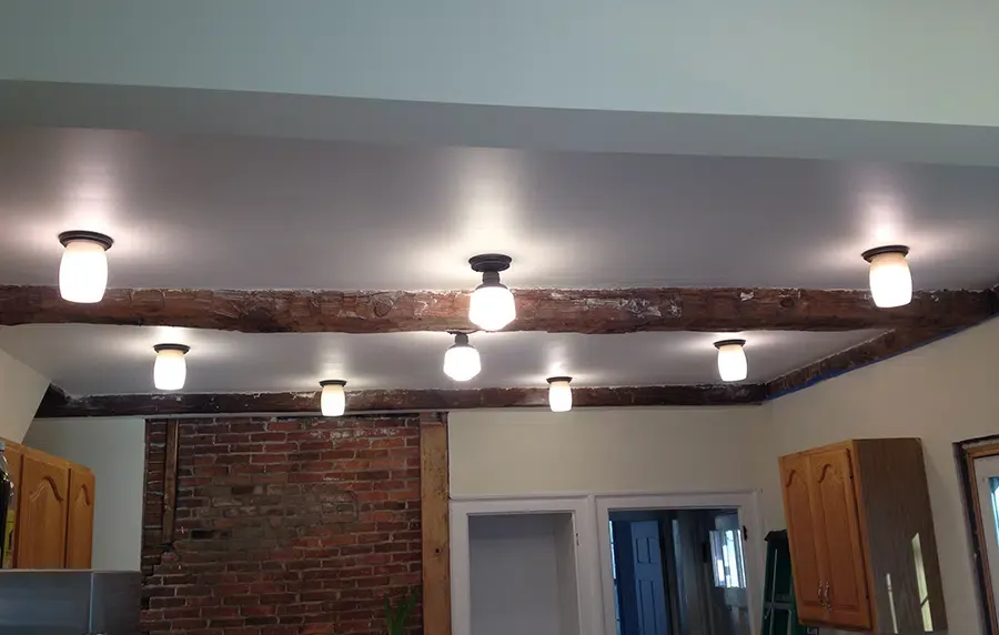 Six flush-mount globe lights installed across exposed beam kitchen ceiling by Castle Electric in Eastern MA