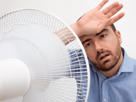 A man cooling off in front of an electric fan during hot weather.