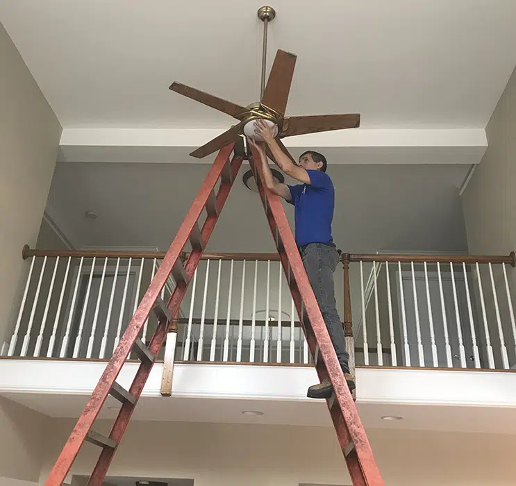 Castle Electric technician installing ceiling fan in Newton MA home from tall A-frame ladder