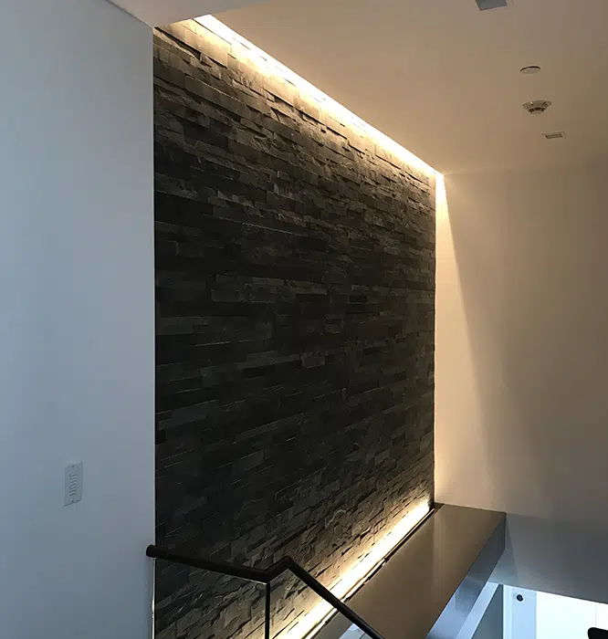 Top and bottom LED cove lighting highlighting a dark stone accent wall by Castle Electric in Eastern MA